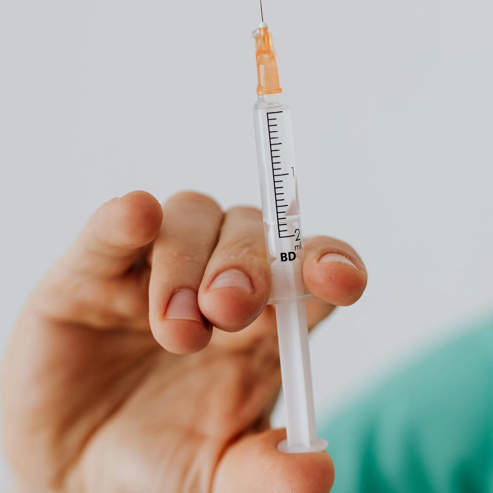 Detailed close-up shot of a hand holding a medical syringe against a neutral background.