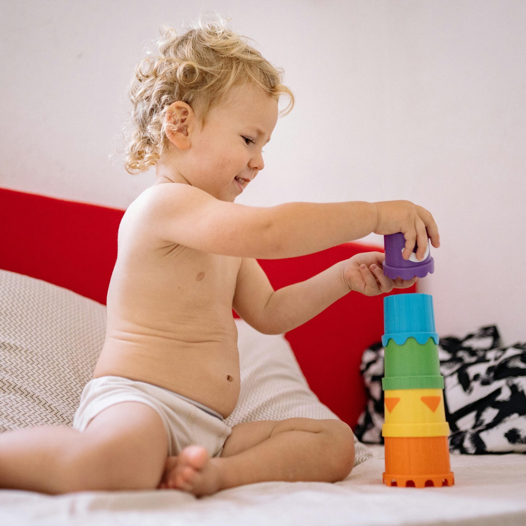 A cheerful toddler building a tower with colorful plastic stacking toys on a sofa.