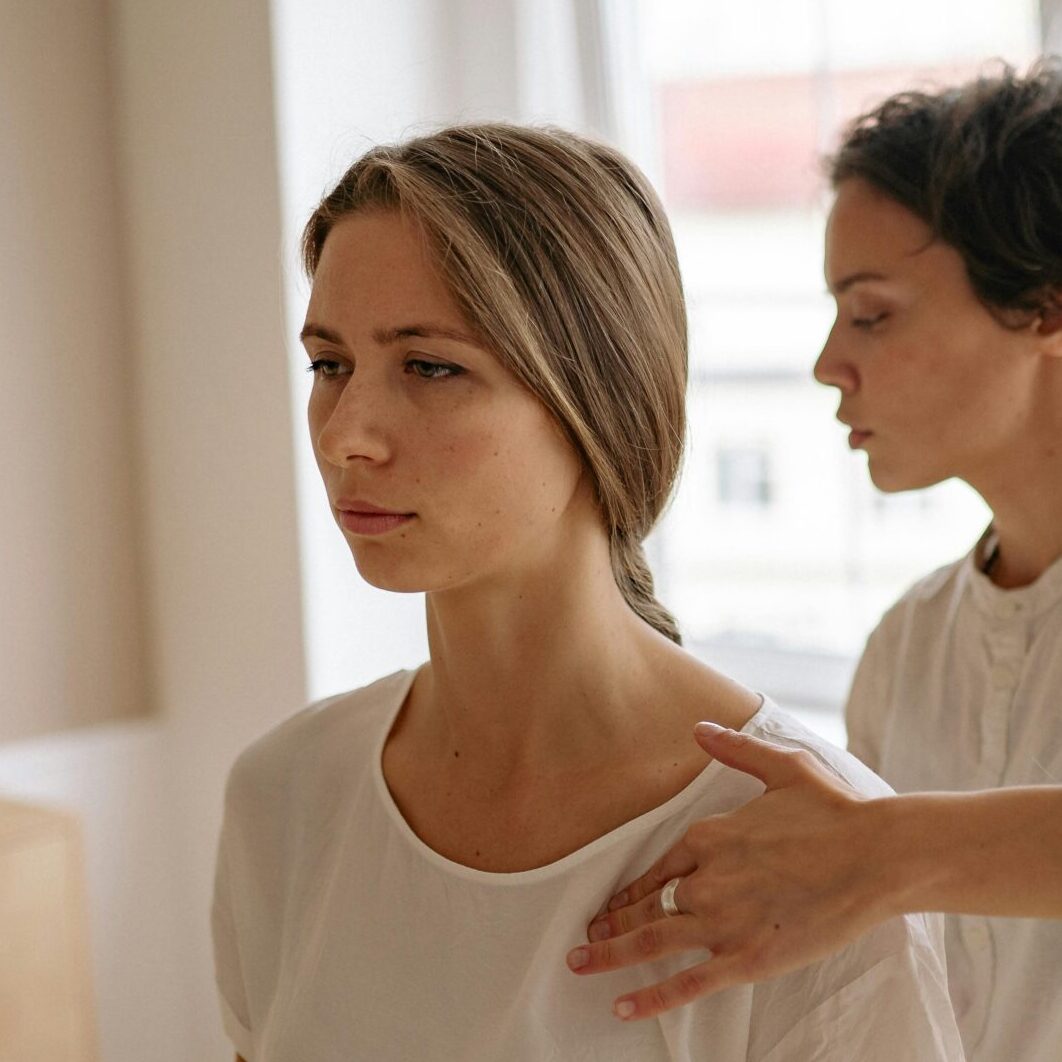 A woman receives shoulder therapy from a therapist in a serene room with natural light.