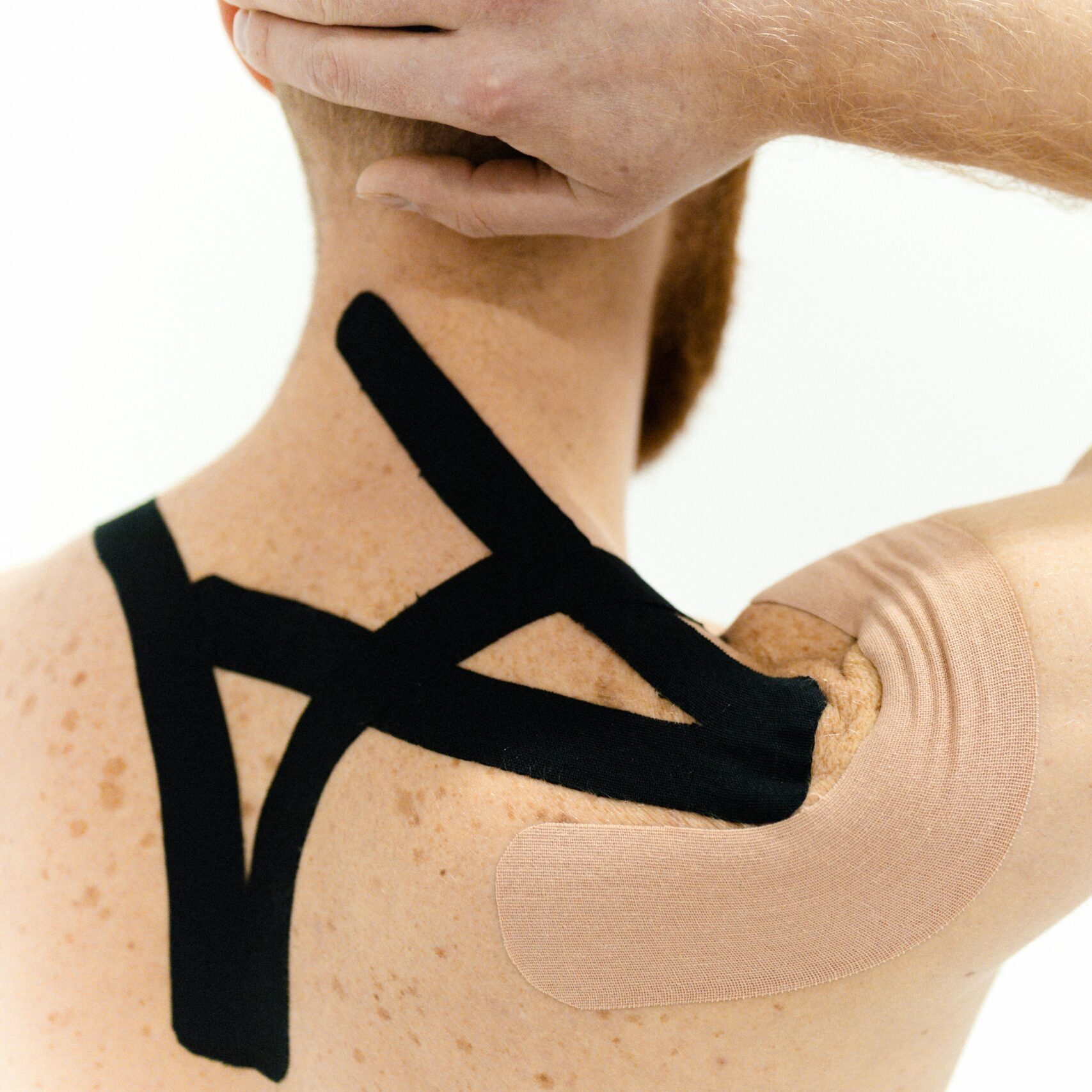 A man with kinesiology tape applied on his shoulder against a white background, showcasing physical therapy support.