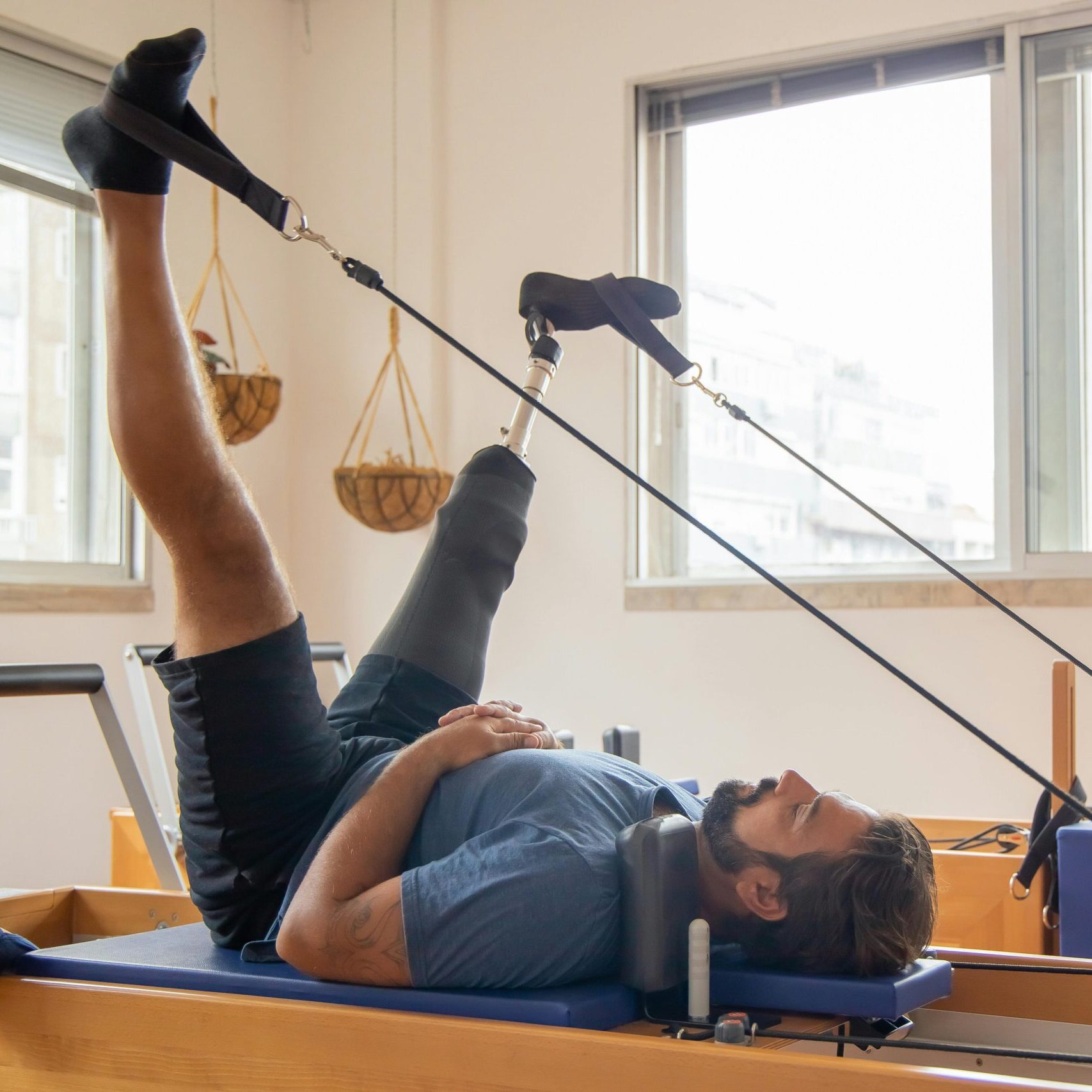Man with prosthetic leg using pilates equipment for physical therapy indoors.