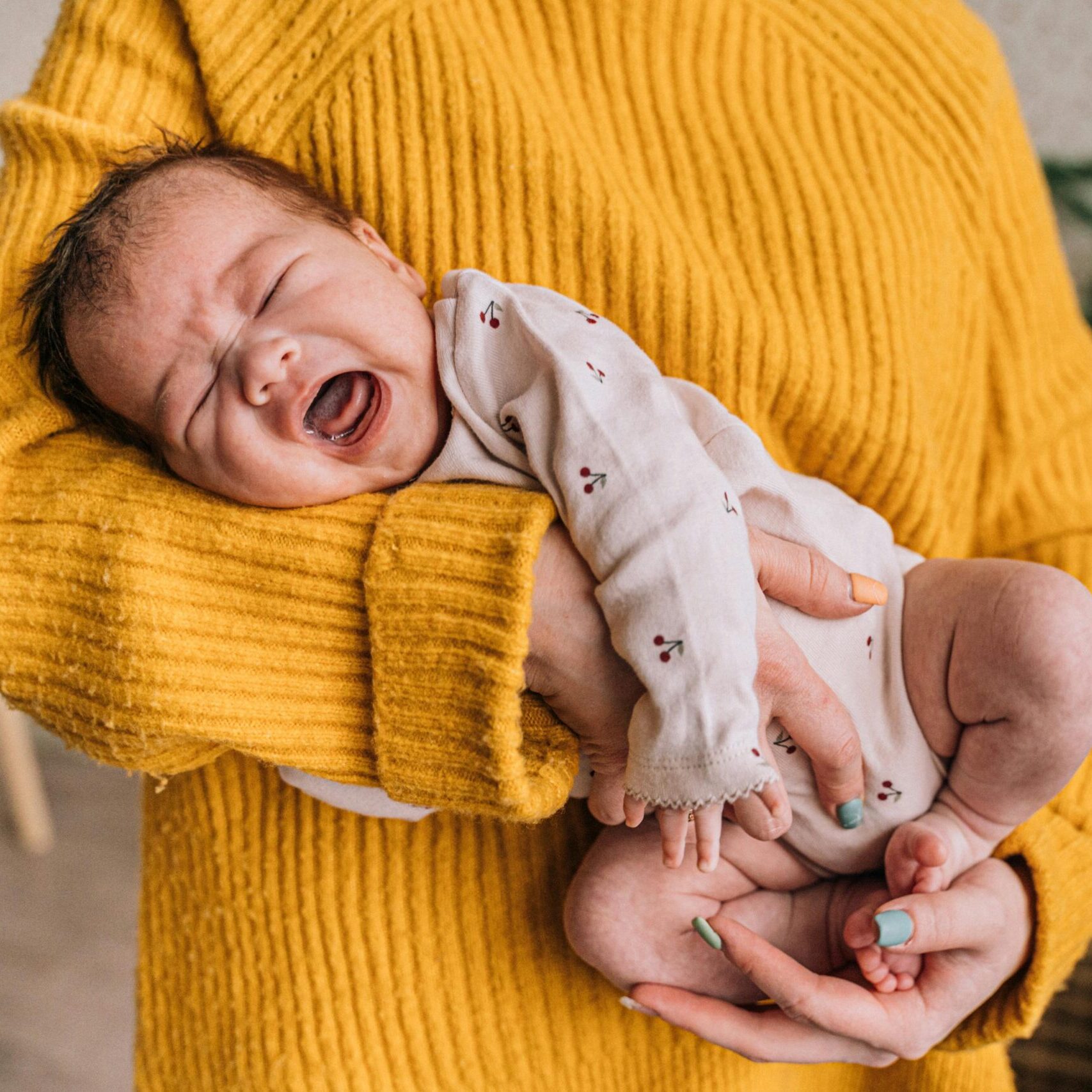 A mother gently holds a crying baby in her arms, providing warmth and comfort indoors.