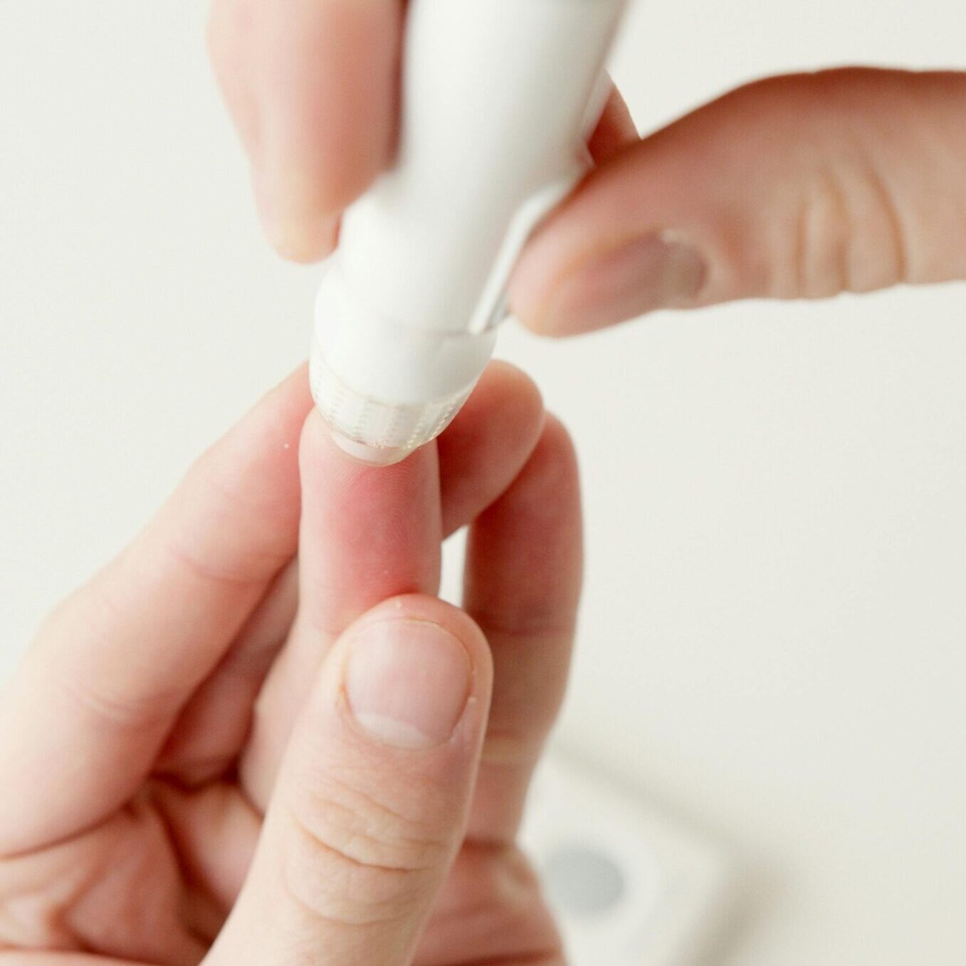 A person using a lancet pen to check blood sugar levels at home.