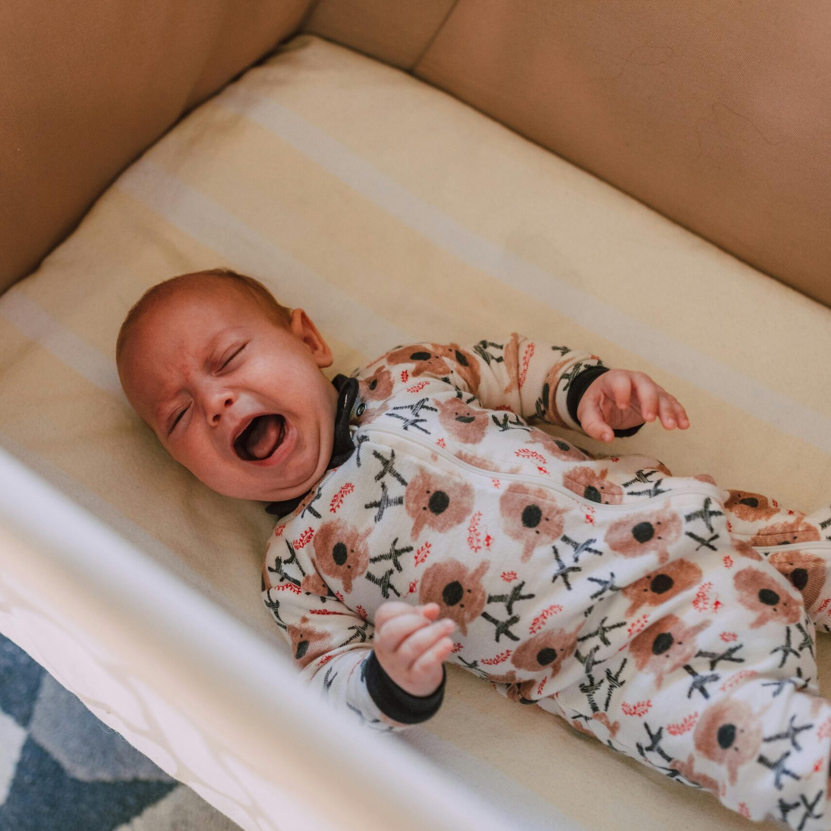 A cute baby in a floral onesie crying in a cozy crib, viewed from above.