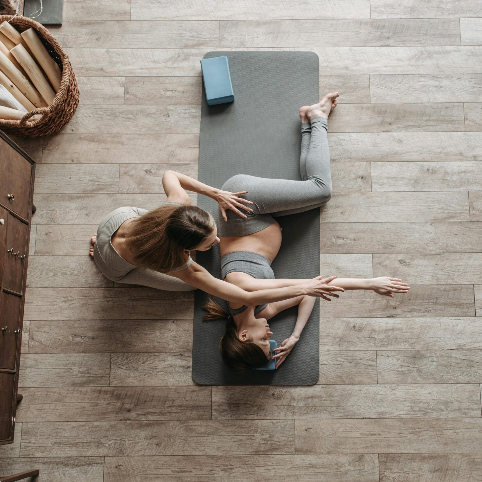 Overhead view of a yoga instructor helping a woman stretch on a mat during an indoor session.
