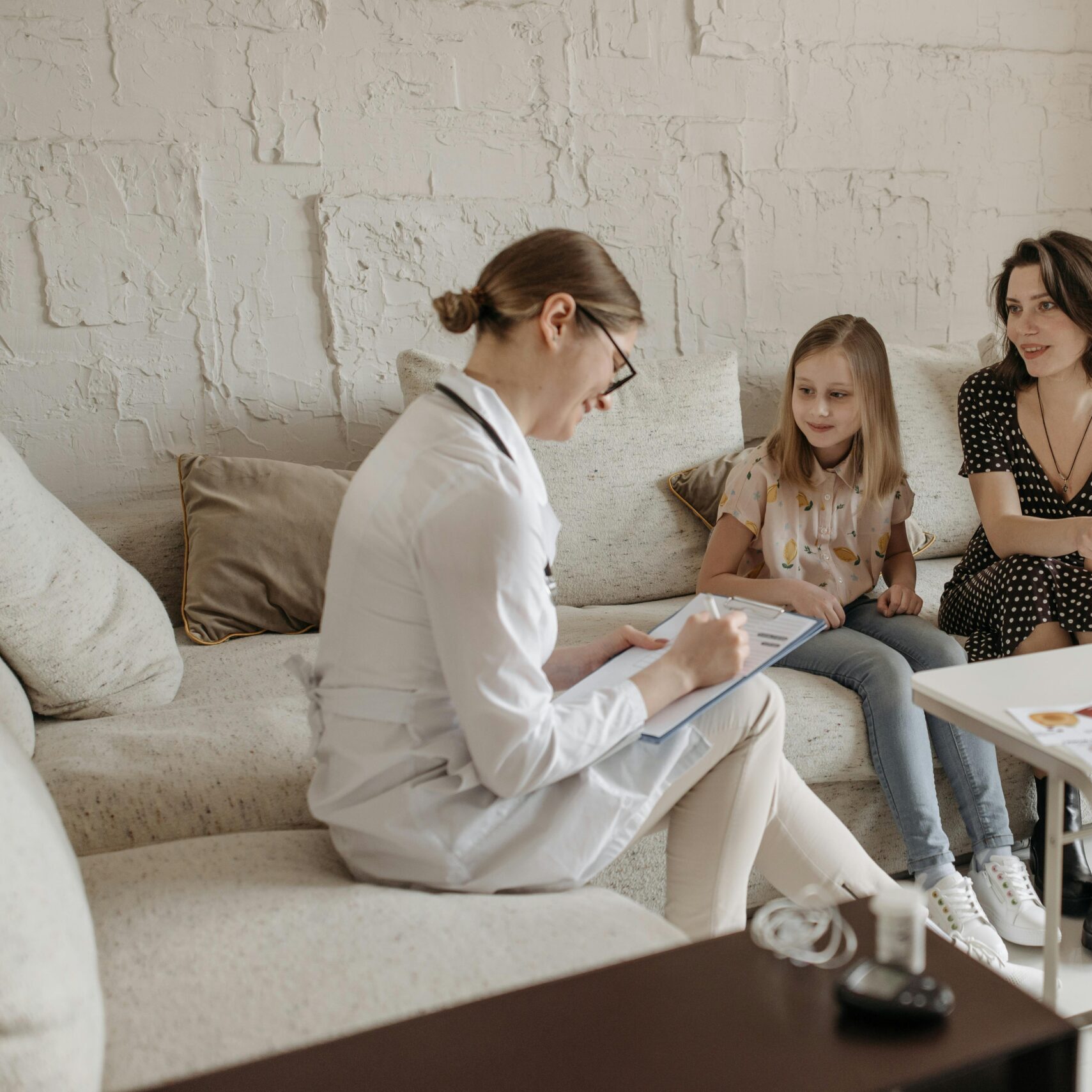 A doctor consults with a mother and daughter in a cozy indoor setting.
