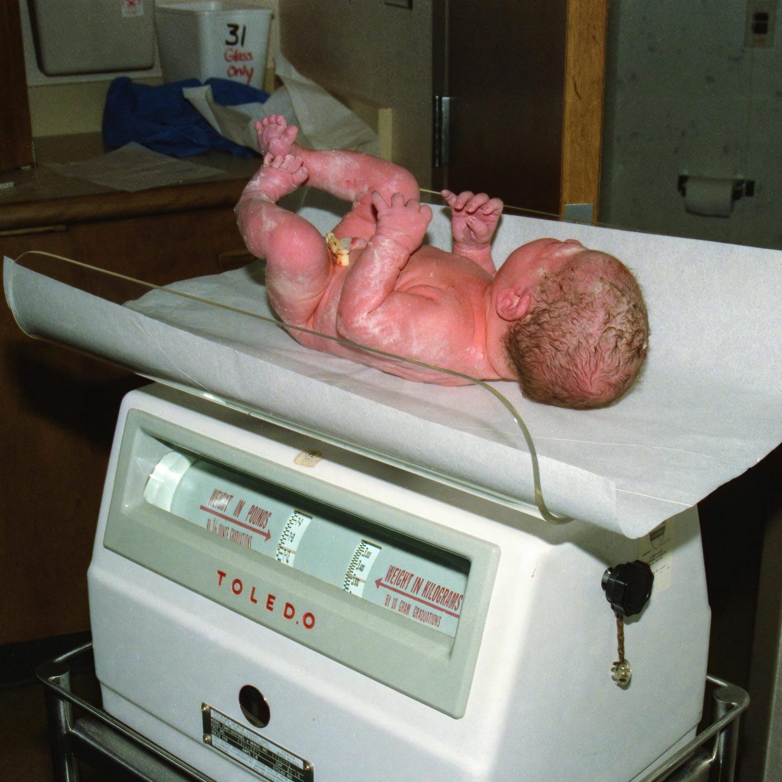 Newborn baby being weighed on a hospital scale, documenting the first moments of life.