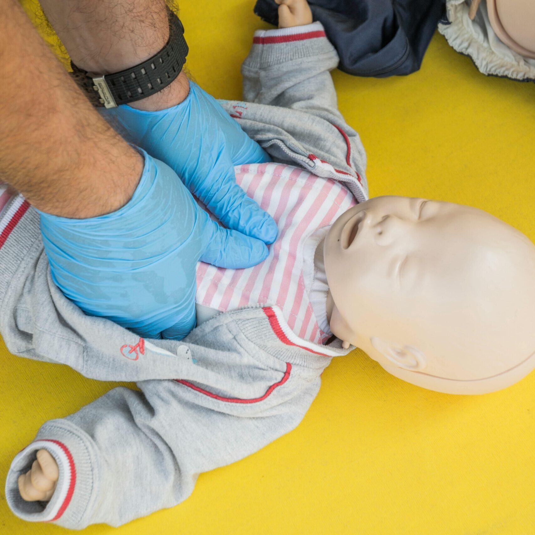 Hands performing CPR on an infant mannequin for a first aid training session.