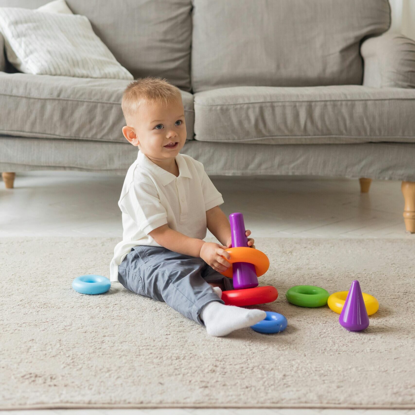 Cute infant plays with vibrant toy rings on the living room floor in a cozy home.