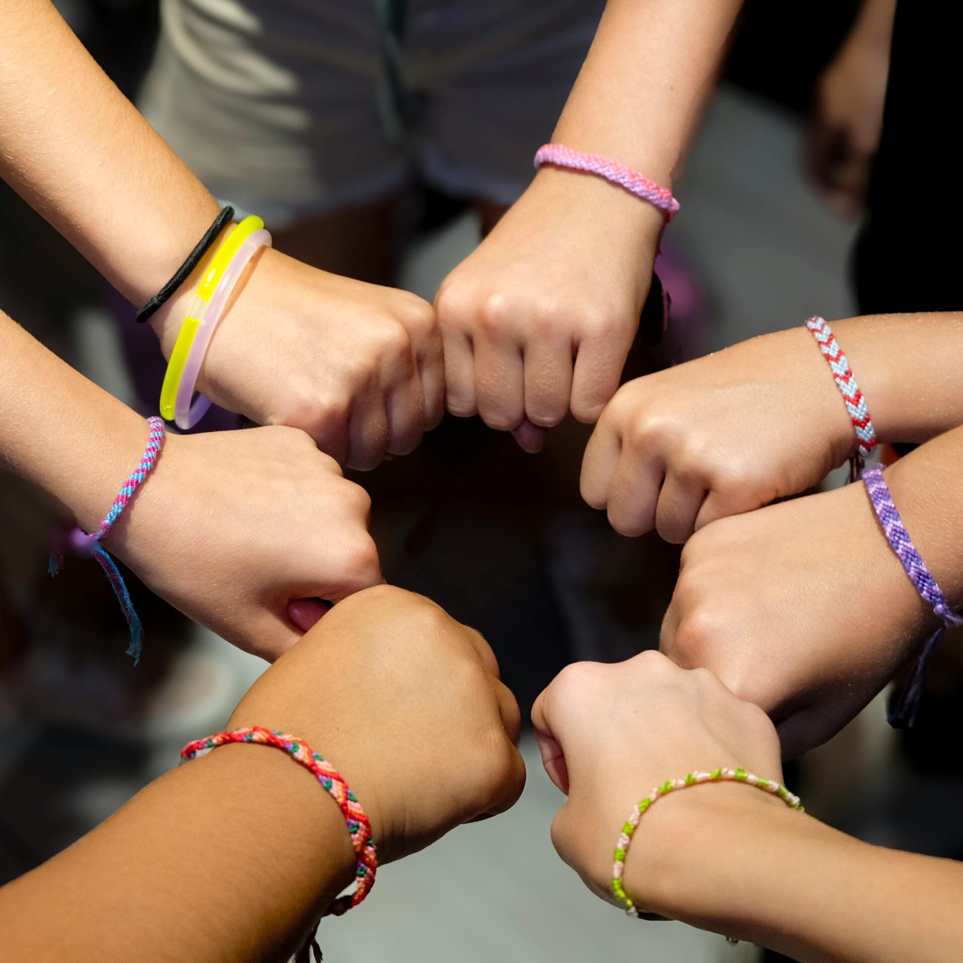 A diverse group of hands wearing colorful friendship bracelets in unity.