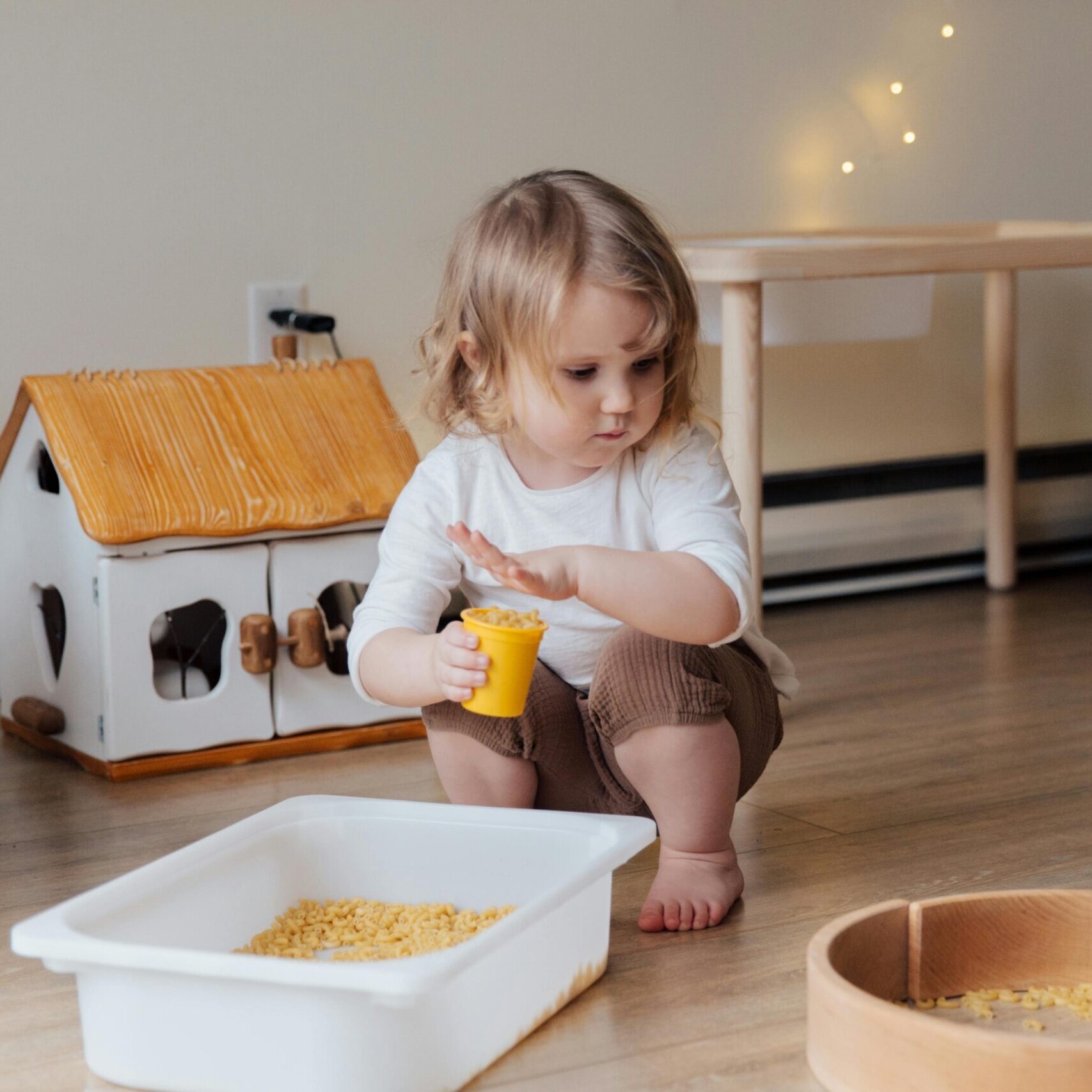 A young child playing with macaroni in a cozy indoor playroom setting.