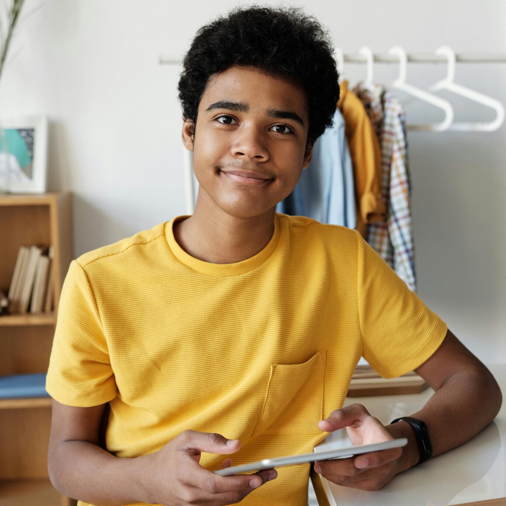 Happy teenage boy sitting indoors using a tablet for online learning.
