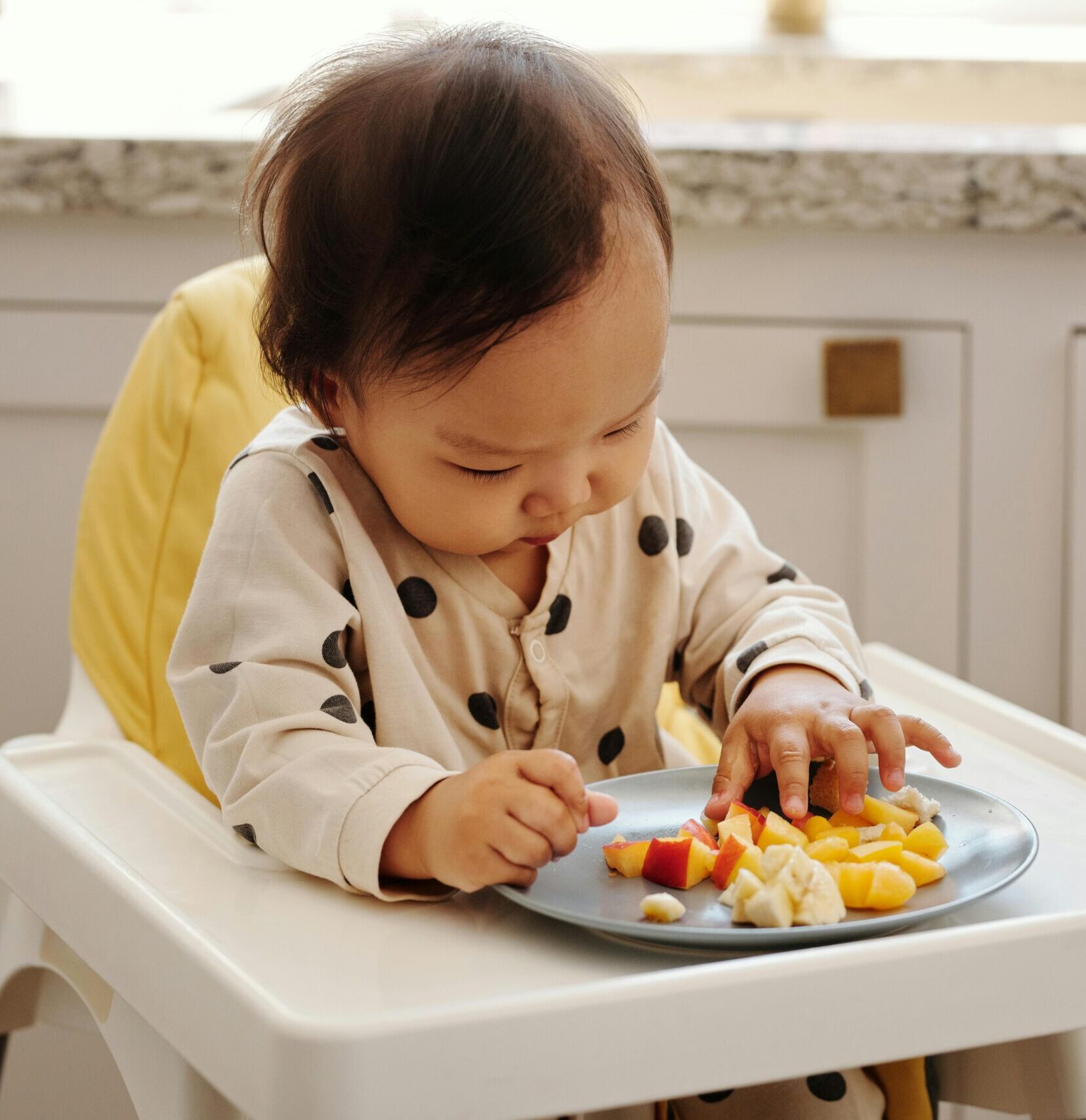 A cute toddler in a polka dot outfit enjoying a healthy fruit snack indoors.