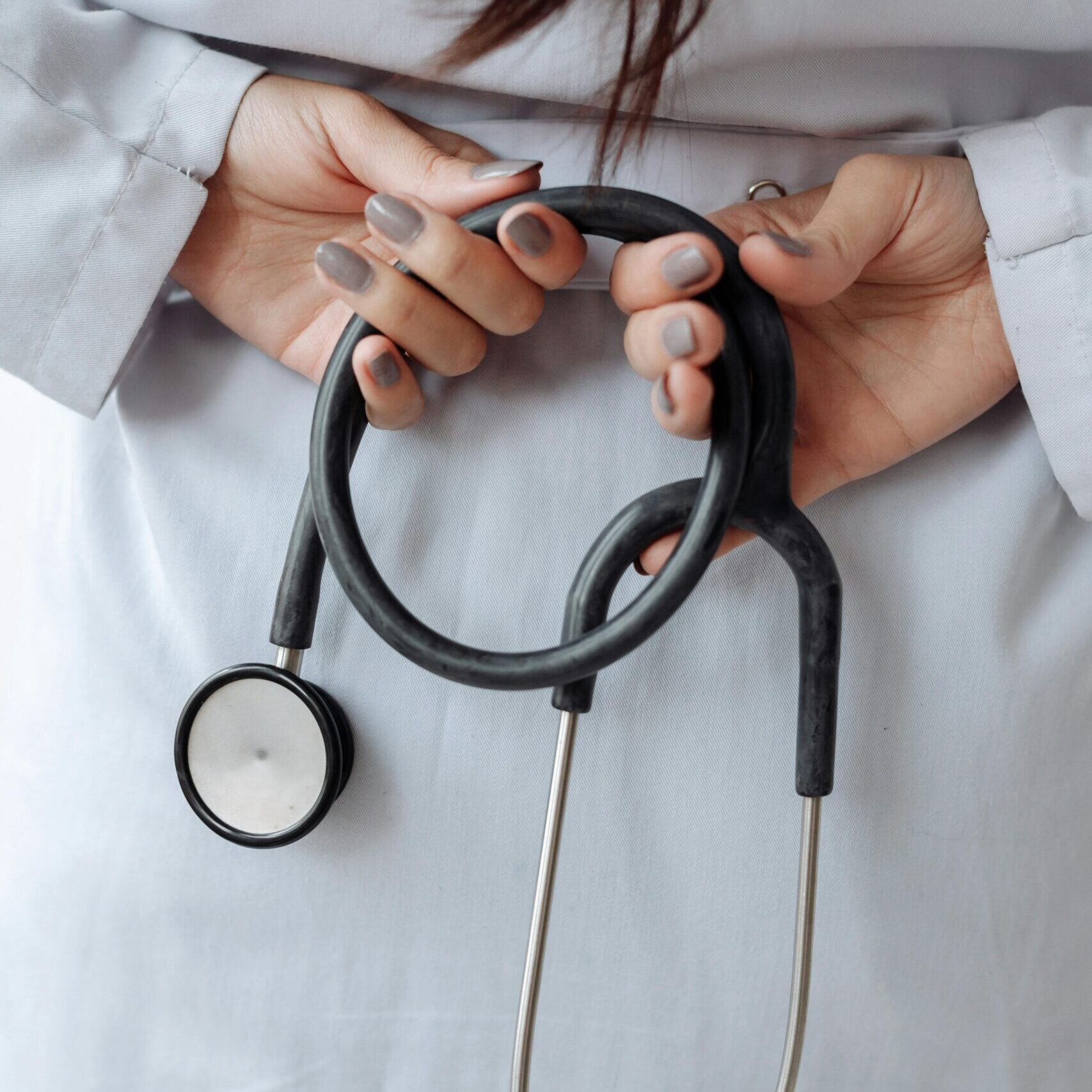 Close-up shot of a doctor holding a stethoscope with both hands, wearing a white coat.