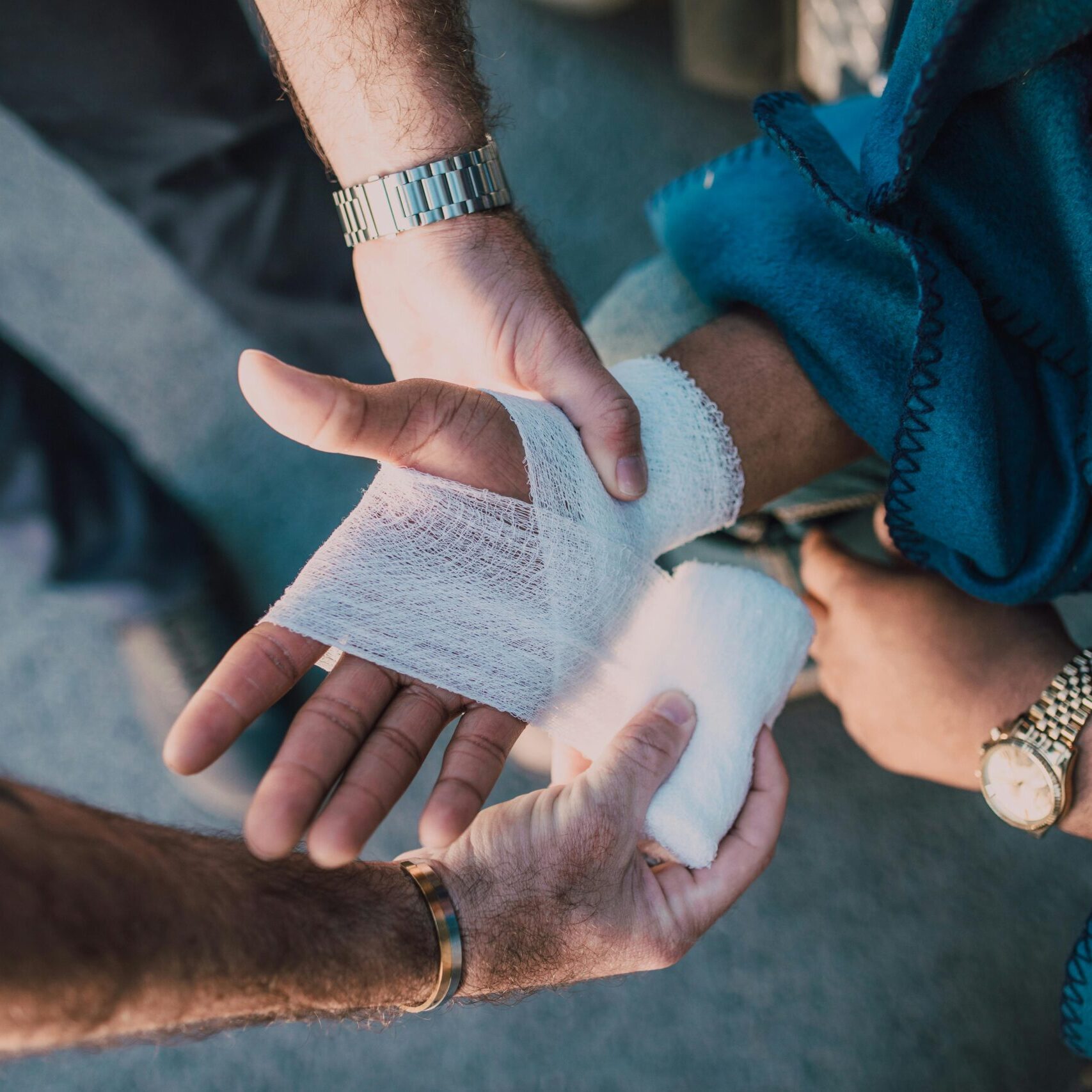 Close-up of two people bandaging an injured hand outdoors, focusing on first aid care.
