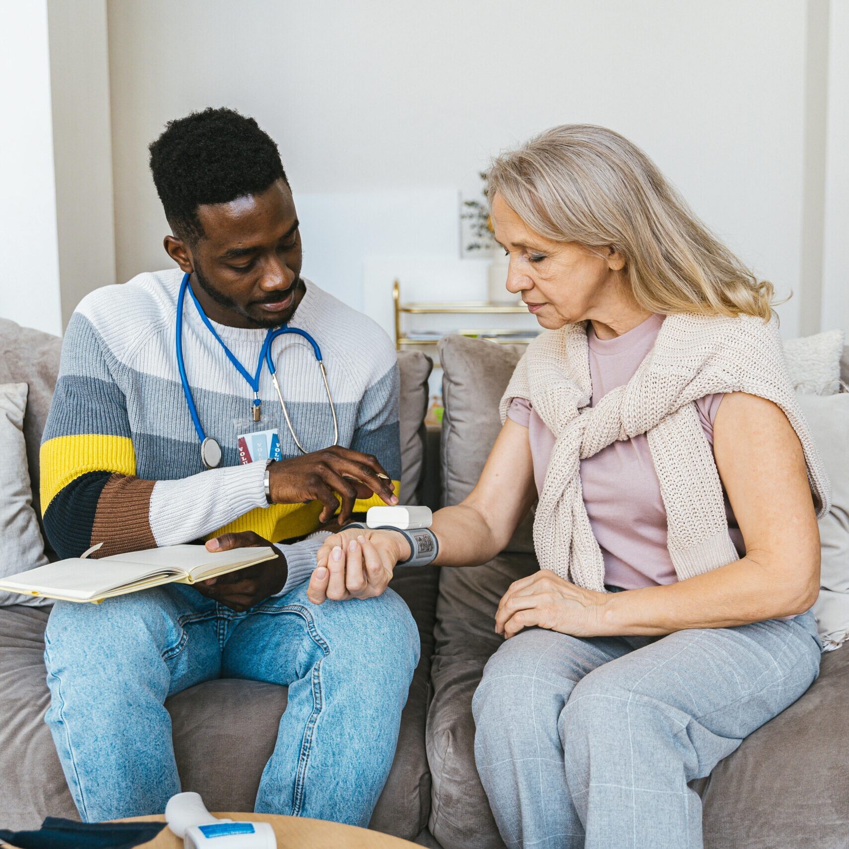 Healthcare professional checking blood pressure of elderly woman in a cozy indoor setting.