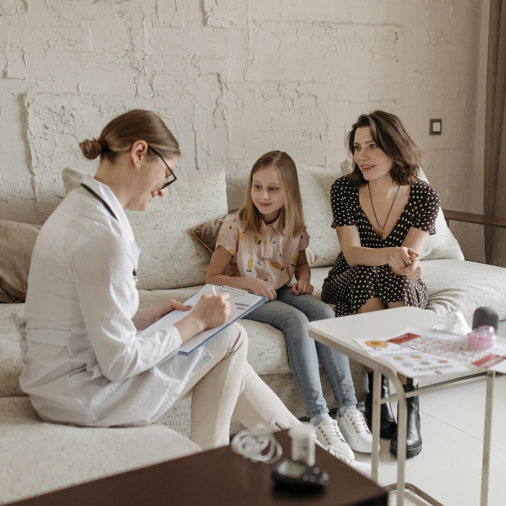 A doctor consults with a mother and daughter in a cozy indoor setting.