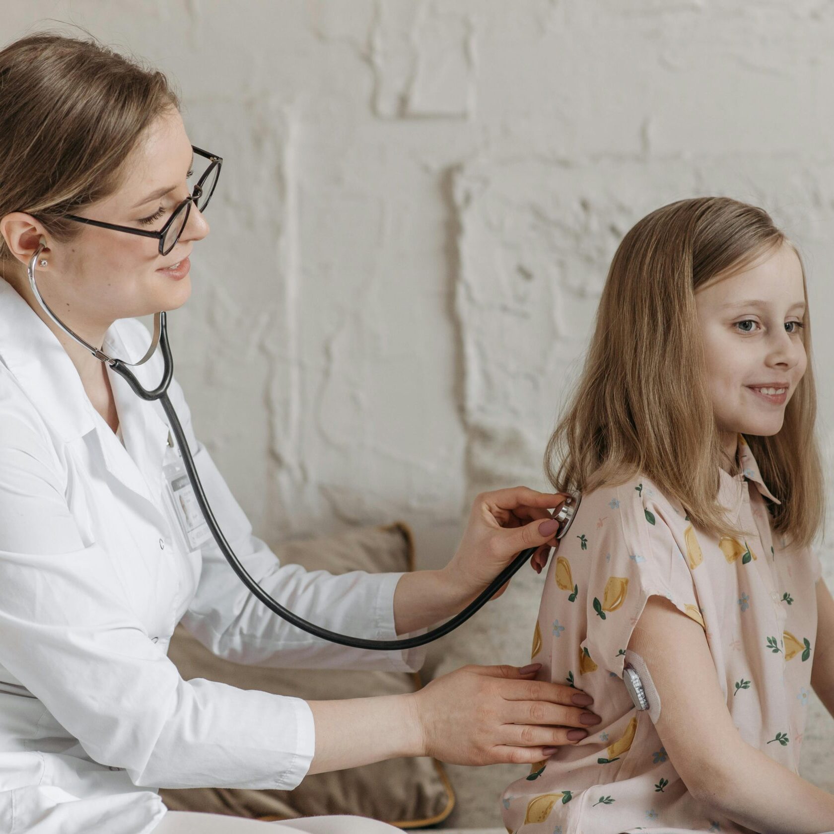 A doctor uses a stethoscope during a check-up with a young girl in a medical setting.