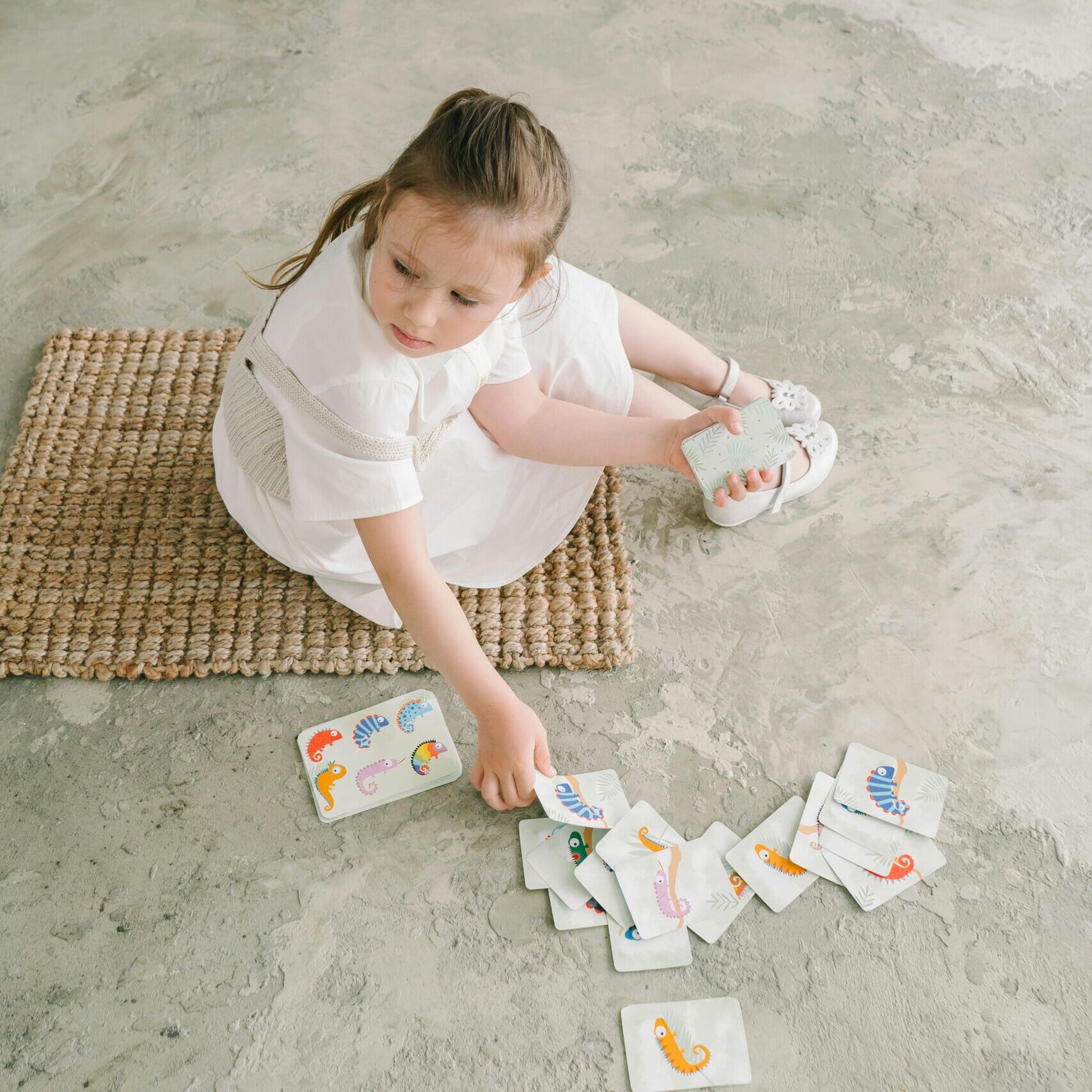 Young girl engaging in developmental learning using visual cards on a woven mat.